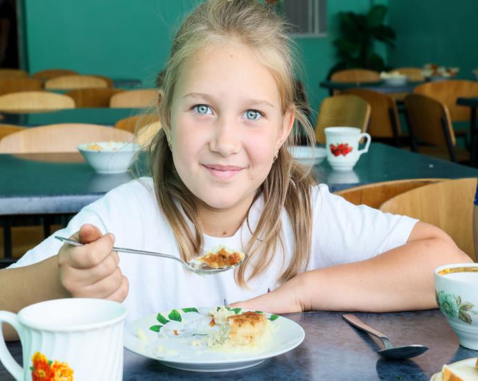 A girl at a table, smiling while holding a spoon