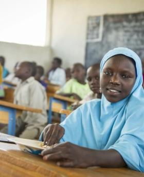 A young student sits at a desk in a classroom.